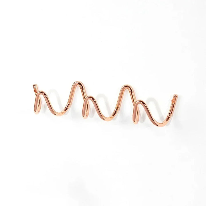 Rose gold wavy wall hook rack with multiple curves, mounted on a white wall.
