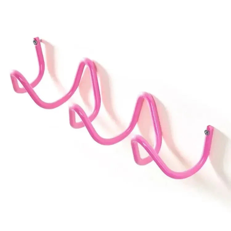 Pink wrought iron wall hook rack with a wavy, serpentine design, mounted on a white wall.