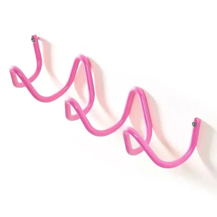 Pink wrought iron wall hook rack with a wavy, serpentine design, mounted on a white wall.