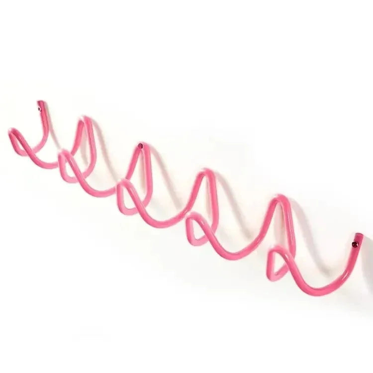 Pink wavy metal wall hook rack with five curves mounted on a white wall.