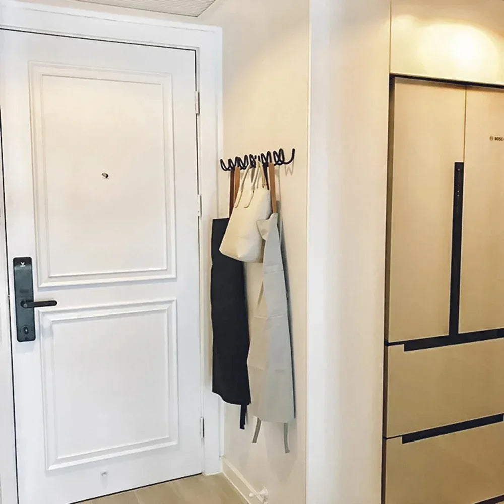 Wrought iron wall hook rack with an ocean wave design, holding aprons and bags.