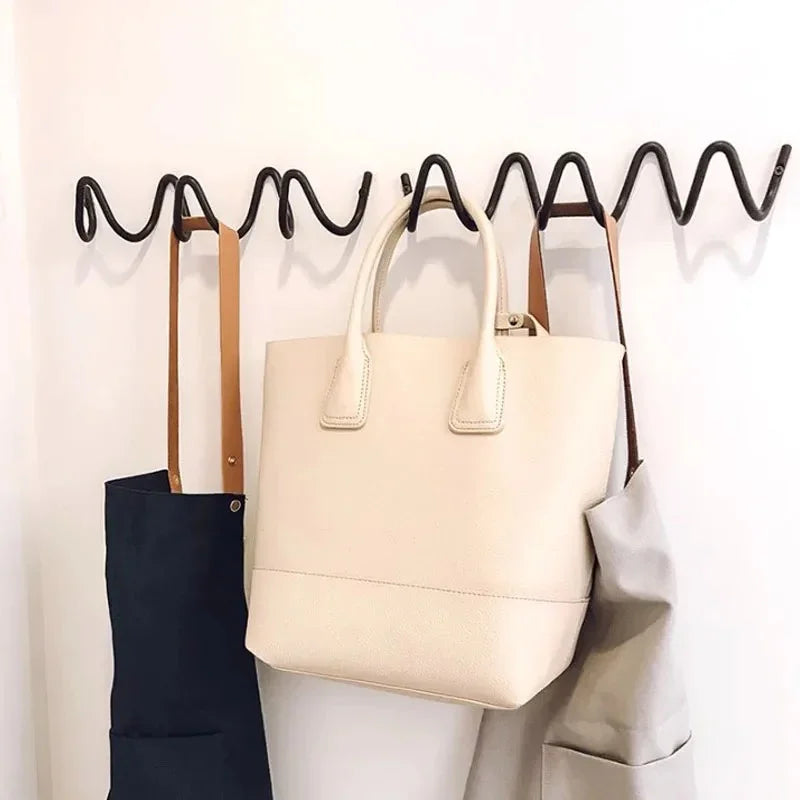 Wrought iron ocean wave wall hook rack with a cream tote bag, navy apron, and grey apron hanging.