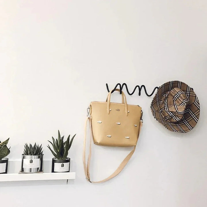 Wrought iron ocean wave wall hook rack with a beige tote bag and a plaid hat hanging on it.