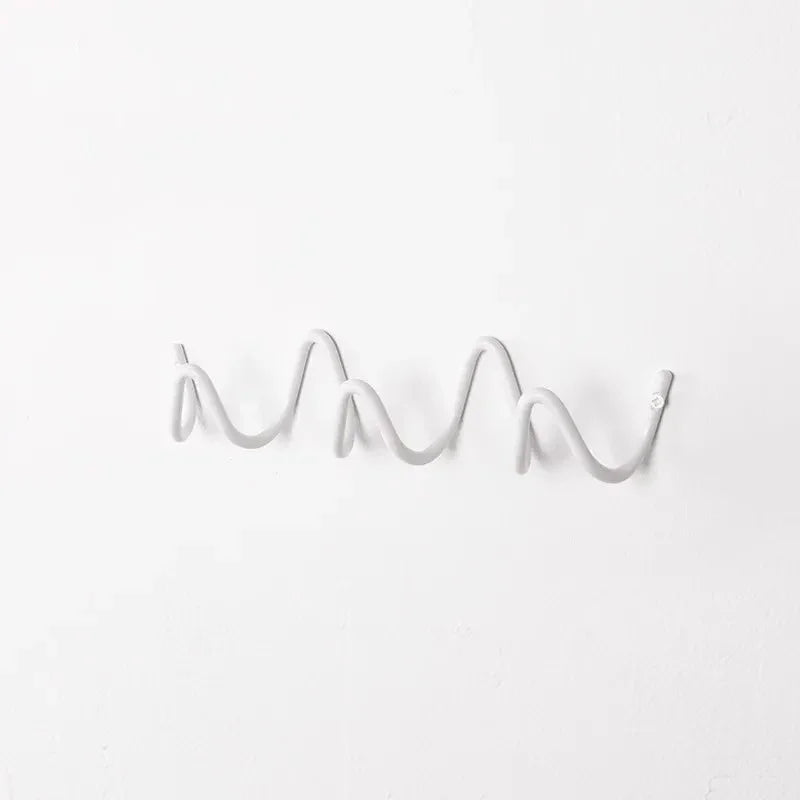 Wrought iron wall hook rack with a wavy, ocean-inspired design in a light gray color.