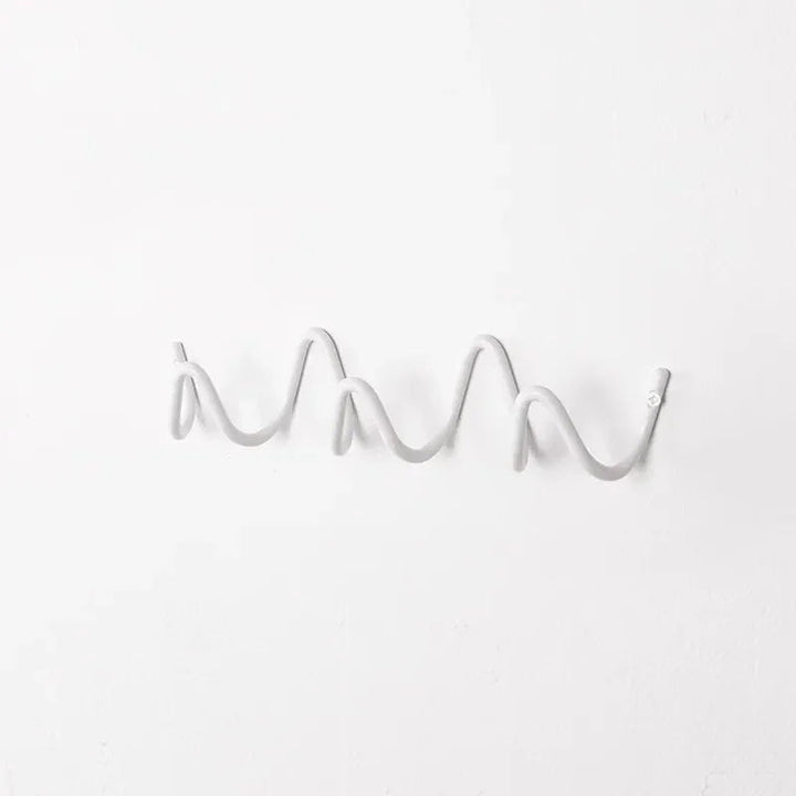 Wrought iron wall hook rack with a wavy, ocean-inspired design in a light gray color.