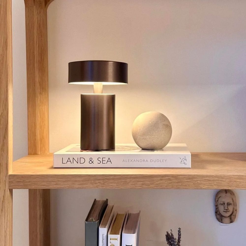 A bronze column LED table lamp sits on a book next to a stone sphere.