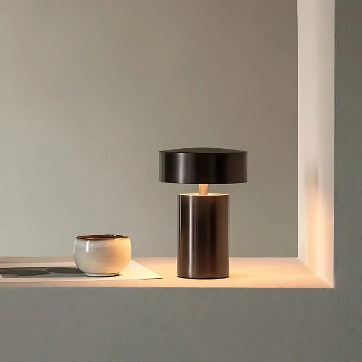 Modern minimalist column LED table lamp with a dark bronze finish and a black shade, casting a warm glow.