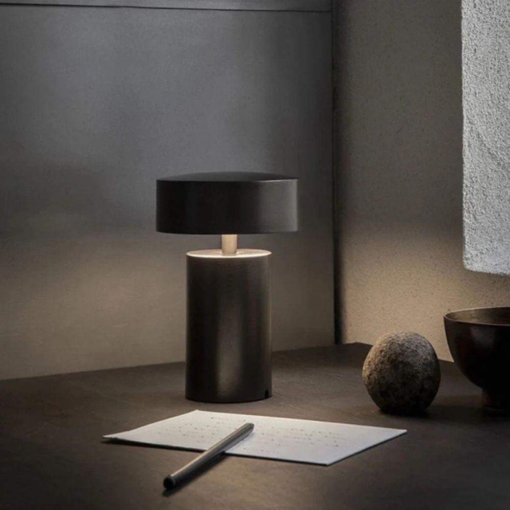 Modern black column LED table lamp with a warm ambient glow on a desk.