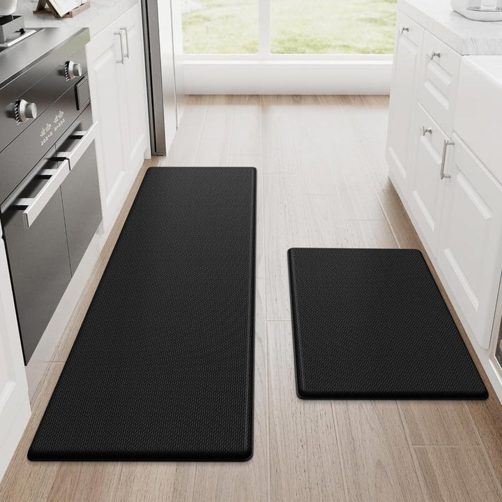 Two black anti-fatigue kitchen mats on a wooden floor, one long runner and one smaller rectangular mat.