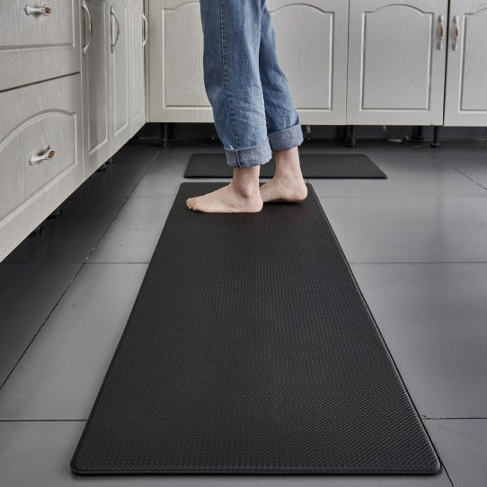 Black anti-fatigue kitchen mat with a textured surface, a person standing on it.