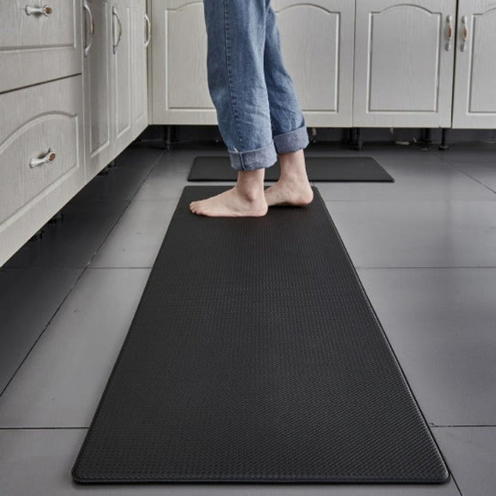 Black anti-fatigue kitchen mat with a textured surface, a person standing on it.