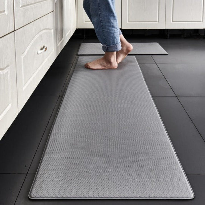 Gray anti-fatigue kitchen mat with a textured surface on a dark tiled floor.