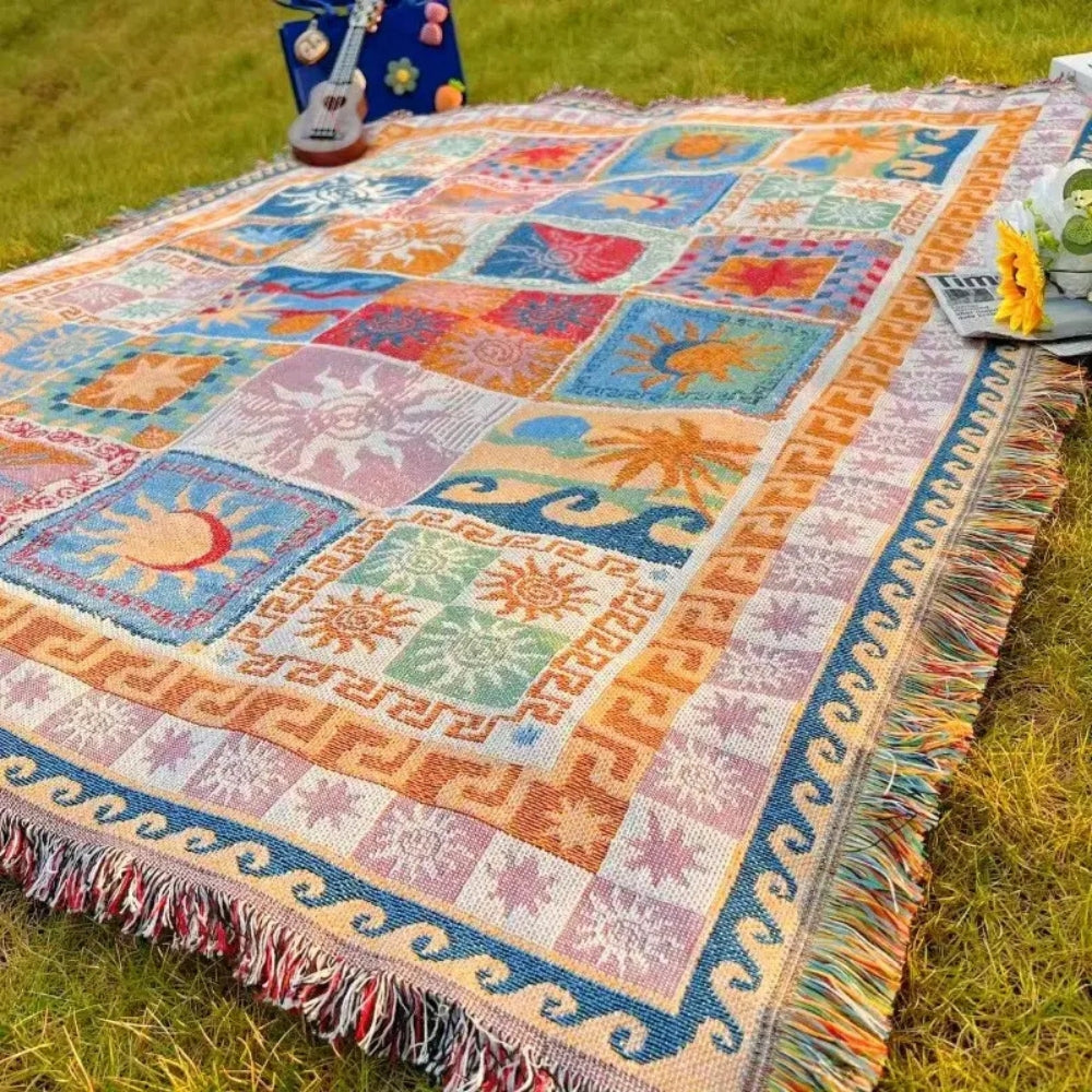 Colorful woven picnic blanket with sun and wave patterns, laid out on grass.