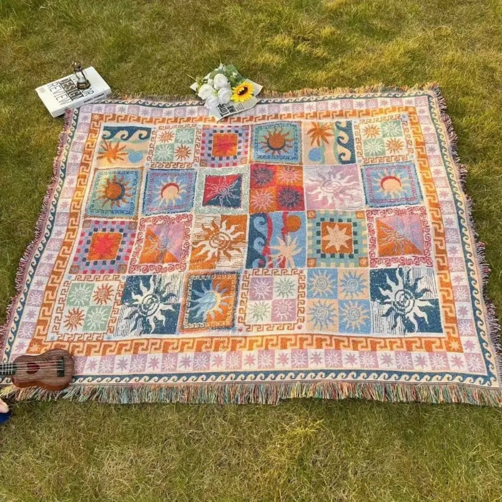 Colorful outdoor picnic blanket with sun patterns and fringe, laid on grass with a ukulele.