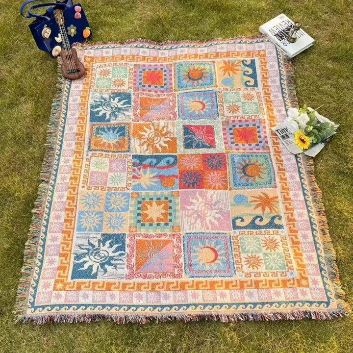 Outdoor picnic blanket with colorful sun and wave patterns on a grassy lawn.