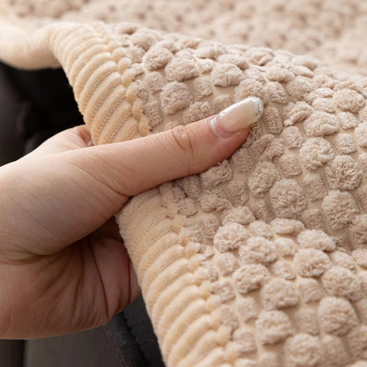 Close-up of a beige quilted sofa cover with a textured geometric pattern, held by a hand.