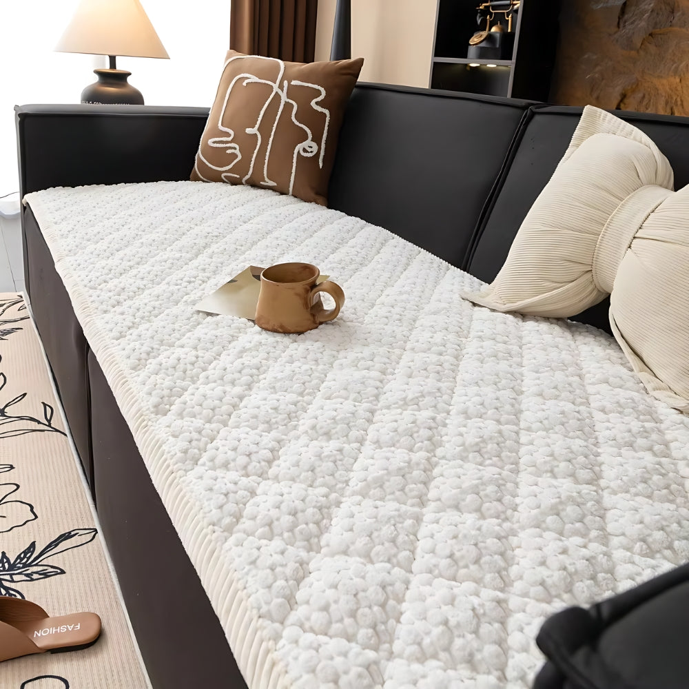 White quilted sofa cover with a textured geometric pattern, featuring a brown mug and a decorative pillow.