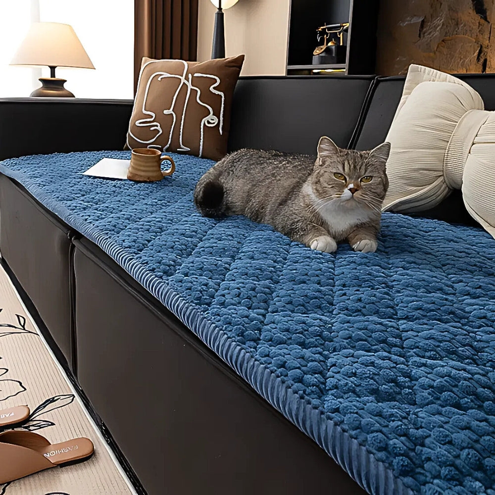 A grey tabby cat rests on a blue quilted sofa cover with a textured geometric pattern.