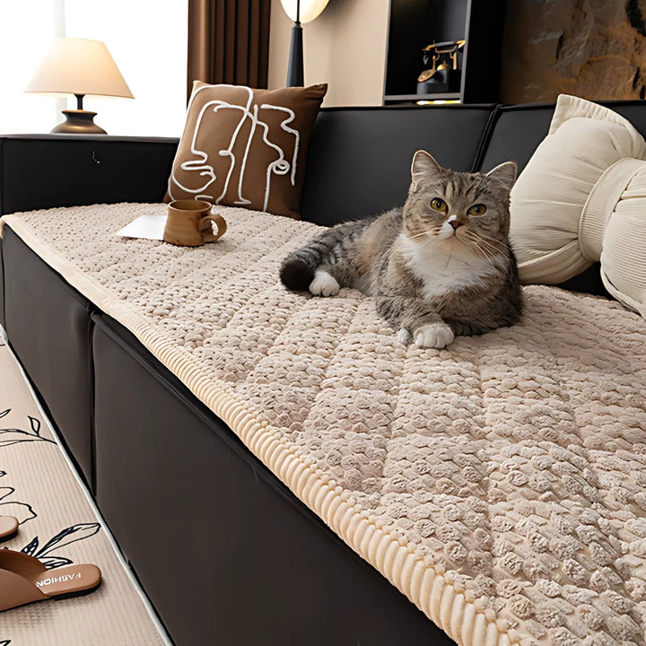 A cat rests on a beige quilted sofa cover with a textured geometric pattern.