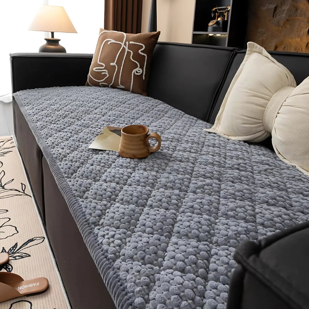 Grey quilted sofa cover with textured pattern, a mug and a book on top.