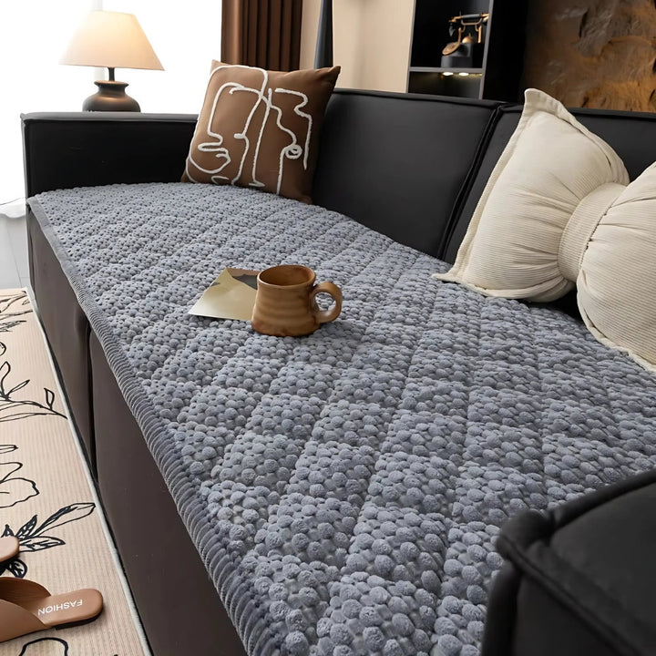 Grey quilted sofa cover with textured pattern, a mug and a book on top.