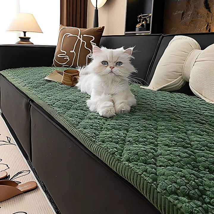 White cat on a green quilted sofa cover with a textured geometric pattern.
