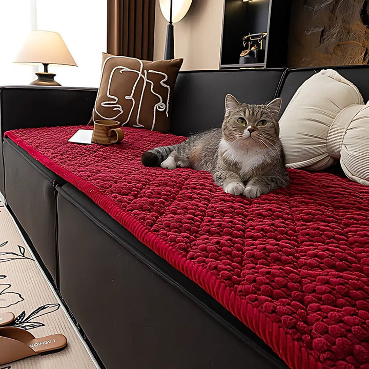 A cat rests on a red quilted sofa cover with a textured pattern.