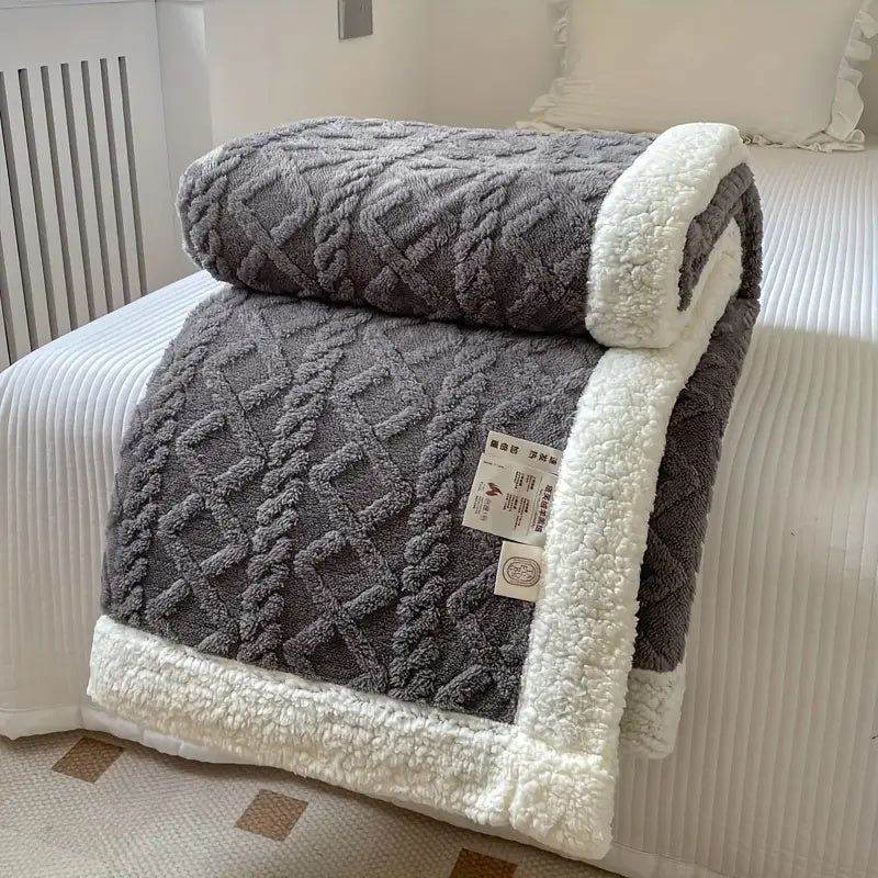 Gray reversible sherpa fleece throw blanket with white sherpa trim folded on a bed.
