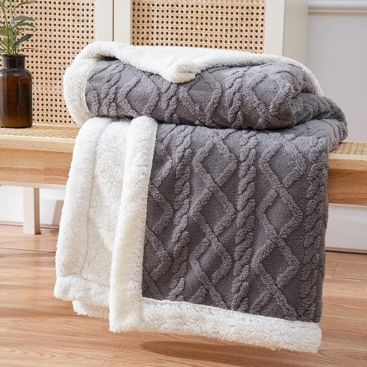 Gray cable knit sherpa throw blanket folded on a wooden bench.
