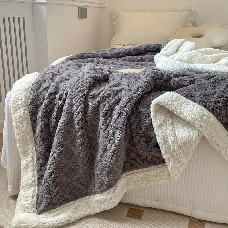 Gray reversible sherpa fleece throw blanket with a textured pattern and white sherpa lining draped on a bed.