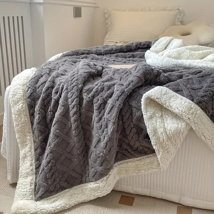 Gray reversible sherpa fleece throw blanket with a textured pattern and white sherpa lining draped on a bed.