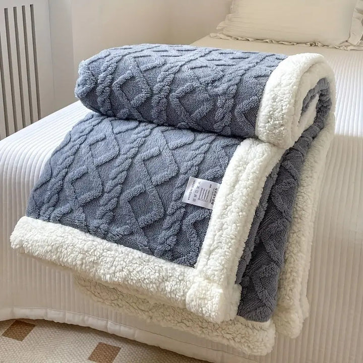 Gray reversible sherpa throw blanket with a cable knit pattern and white sherpa trim, folded on a bed.