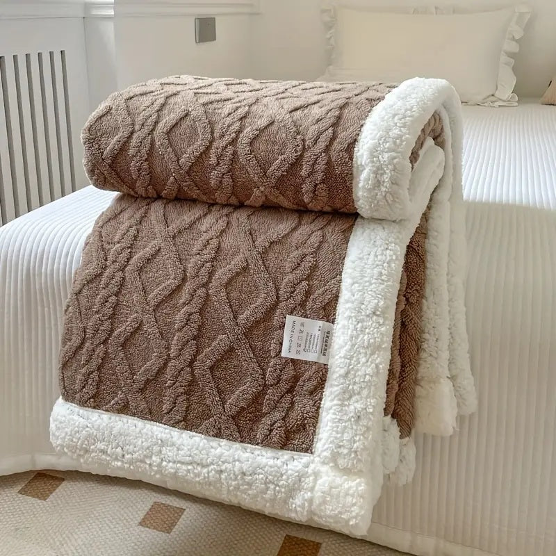 Brown cable knit sherpa throw blanket folded on a bed with white trim.