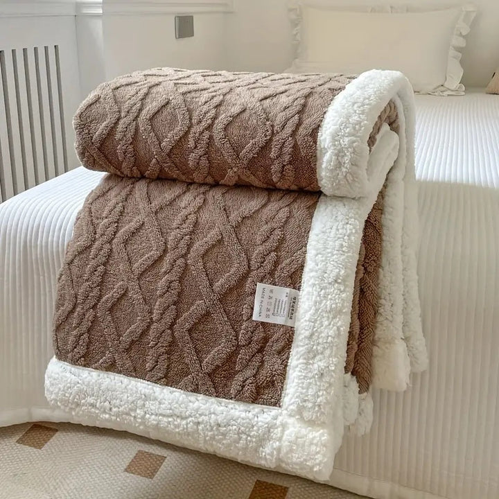 Brown cable knit sherpa throw blanket folded on a bed with white trim.