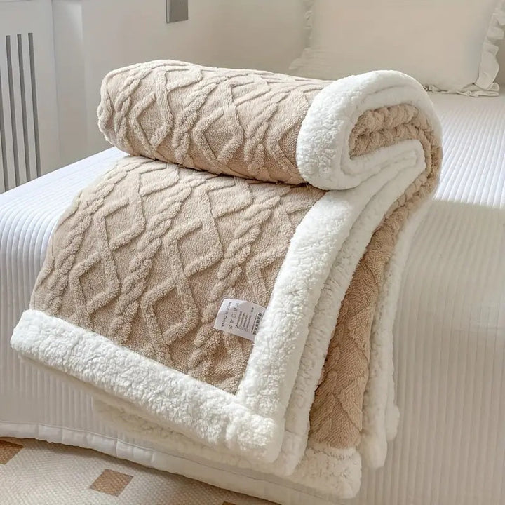 Beige sherpa fleece throw blanket with white sherpa trim, folded on a bed.