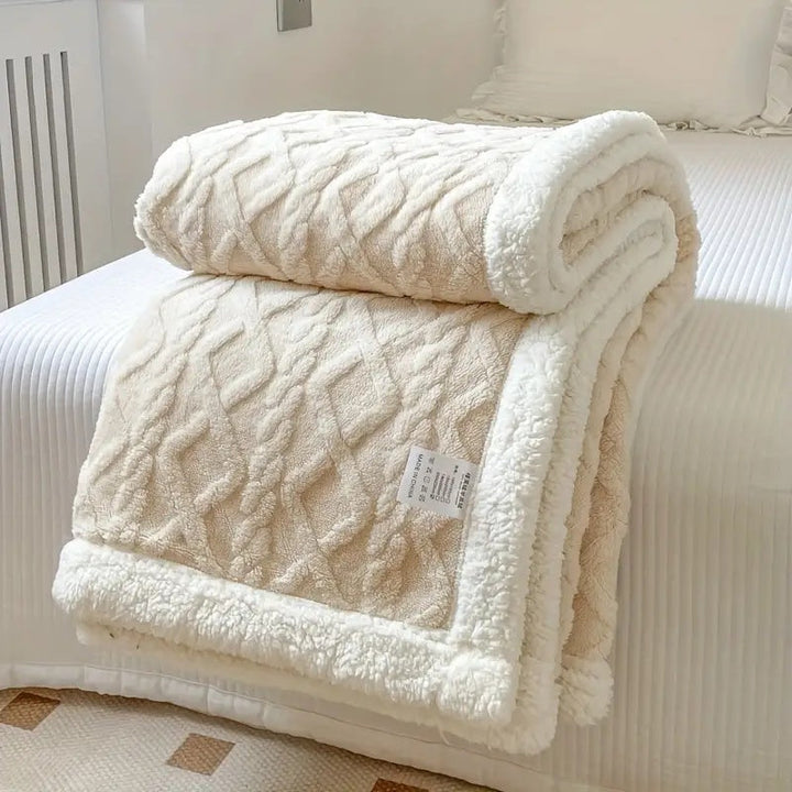 Cream sherpa fleece throw blanket with a diamond pattern, folded on a bed.