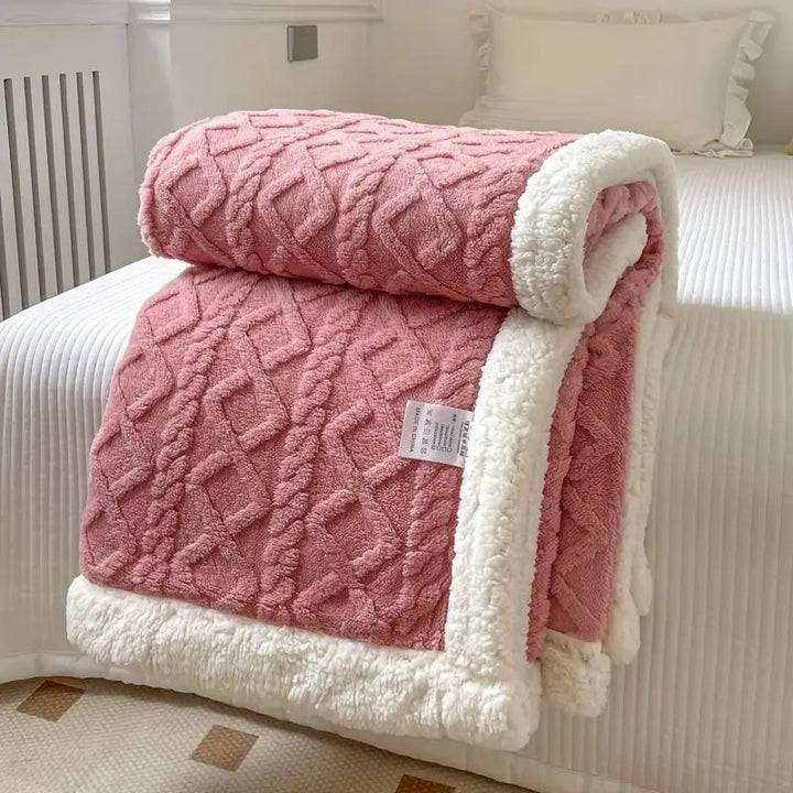 Pink sherpa fleece throw blanket with a cable knit pattern and white sherpa trim, folded on a bed.