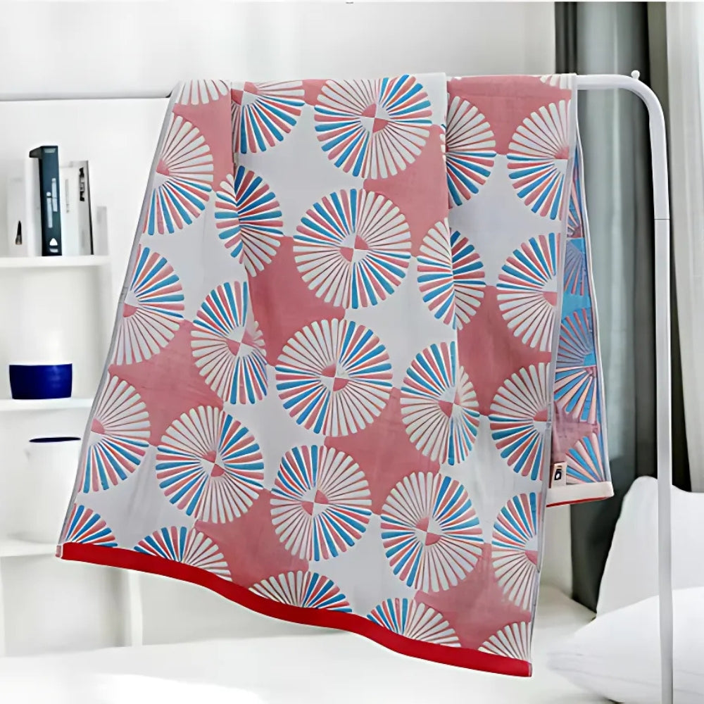 Pink cotton bath towel with a repeating pattern of white, blue, and pink circular fan designs and a red border.