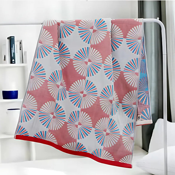 Dahlia Blossom Cotton Bath Towel with a pink background and a repeating pattern of white, blue, and pink fan-like floral designs.