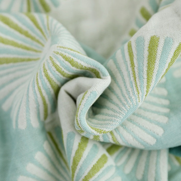 Close-up of a soft, woven jacquard cotton bath towel with a repeating dahlia blossom pattern in green and light blue.