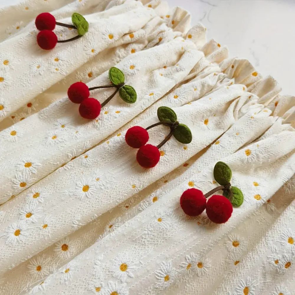 Cream cabinet curtain with embroidered white daisies and red cherry pom-pom accents.