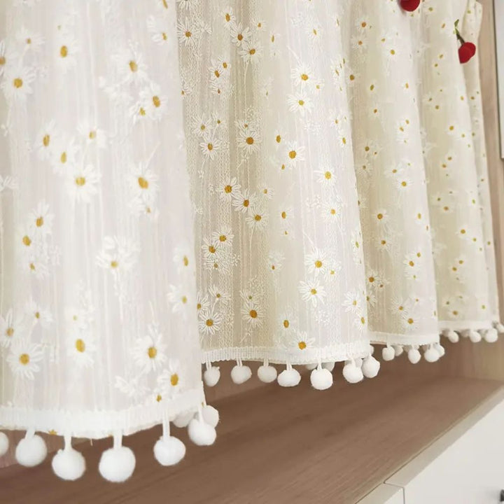 White sheer cabinet curtain with a daisy pattern and white pom-pom trim.