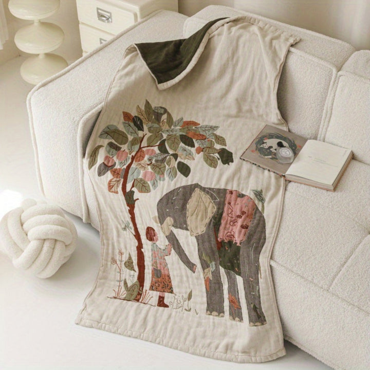A cotton blanket with a printed design of an elephant and a girl under a tree, draped on a sofa.