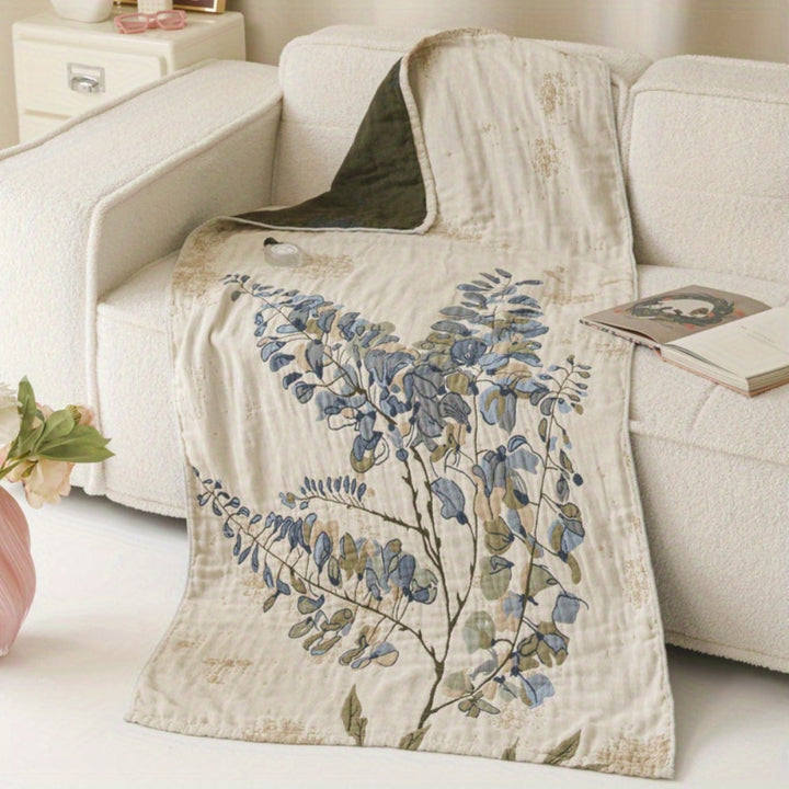 A cotton towel blanket with a vintage floral print in blue and green on a cream background, draped over a white sofa.