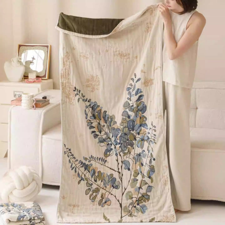 A woman holds up a cream-colored cotton towel blanket with a vintage floral print and a dark green edge.
