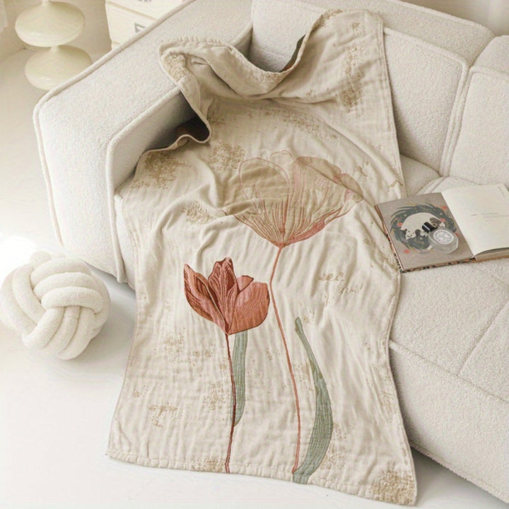 Cotton towel blanket with a vintage floral design in muted pink and green tones, draped over a cream sofa.