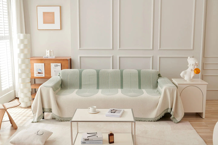 Pistachio green chenille throw blanket with tassels draped over a sofa.