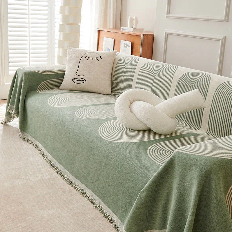 Pistachio green chenille throw blanket with tassels draped over a sofa with decorative pillows.