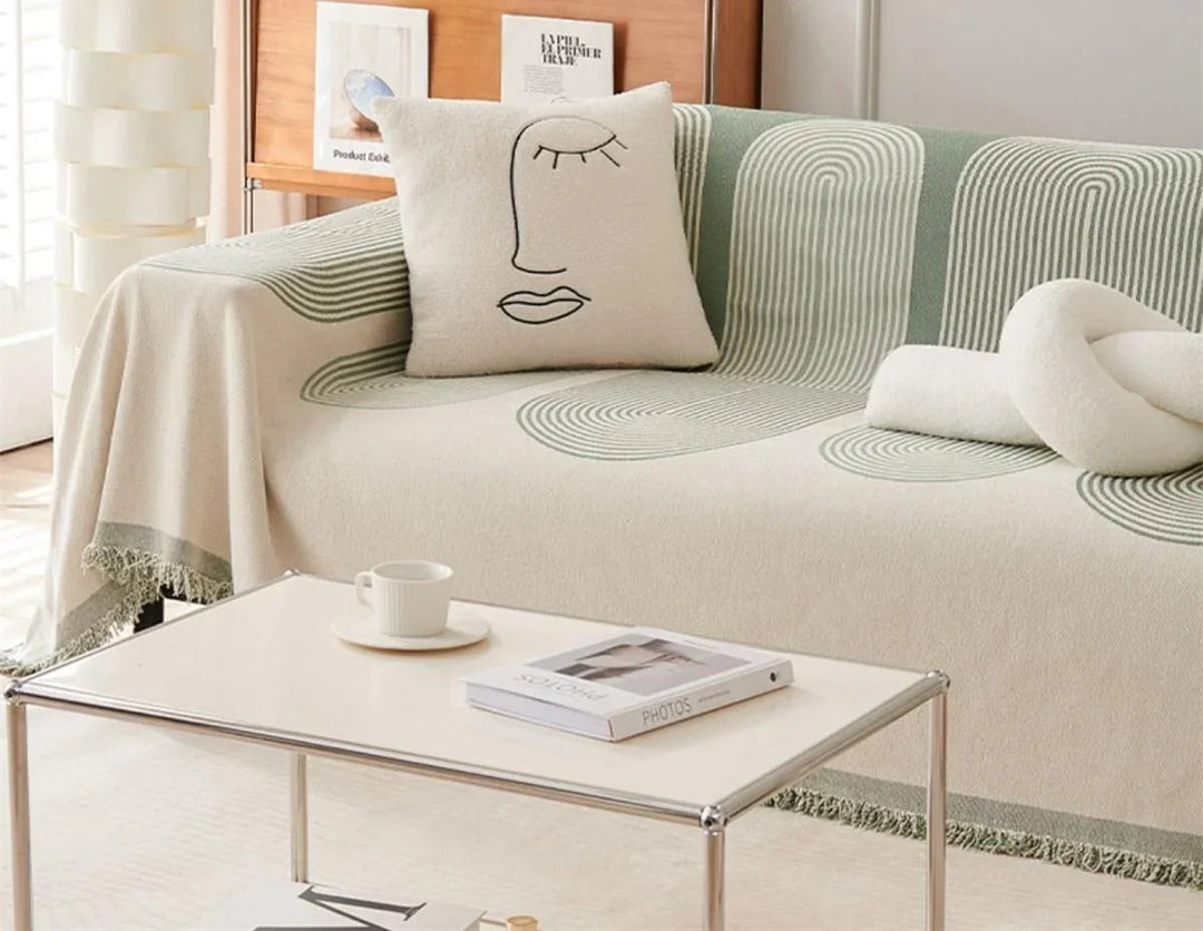 Pistachio chenille throw blanket with tassels draped over a sofa with a decorative pillow and coffee table.
