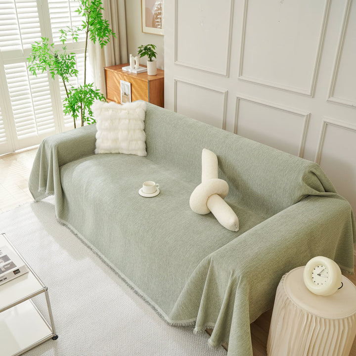 Sage green throw blanket draped over a sofa with decorative pillows and a cup of tea.